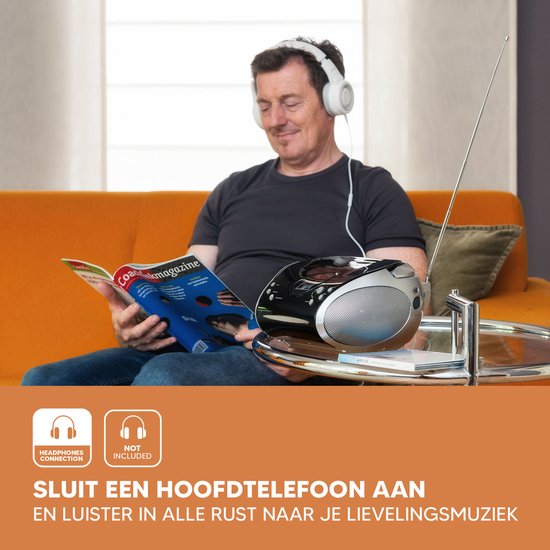 Man met koptelefoon op, leest tijdschrift op oranje bank. Naast hem staat een Lenco radio CD-speler.