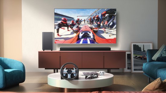 Woonkamer met tv waarop raceauto's te zien zijn, soundbar, subwoofer en race stuur.