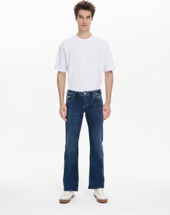 Rechte donkerblauwe jeans met lichte wassing, gedragen door een man met een witte T-shirt en witte sneakers.