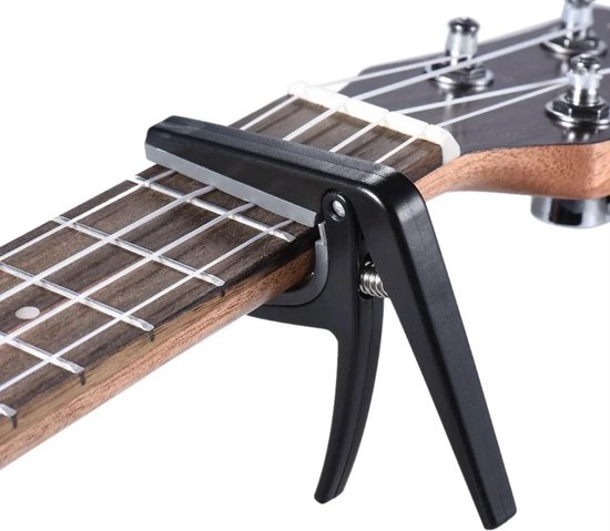 Zwarte capo op de frettenplank van een ukelele, met witte snaren.