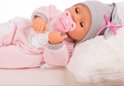 Slapende babypop in roze slaappakje met grijze stippenmuts, liggend op een kussen.