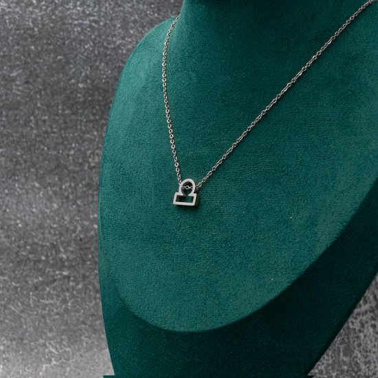 Collier argenté avec symbole Balance (Libra), drapé autour d'un présentoir en velours vert.