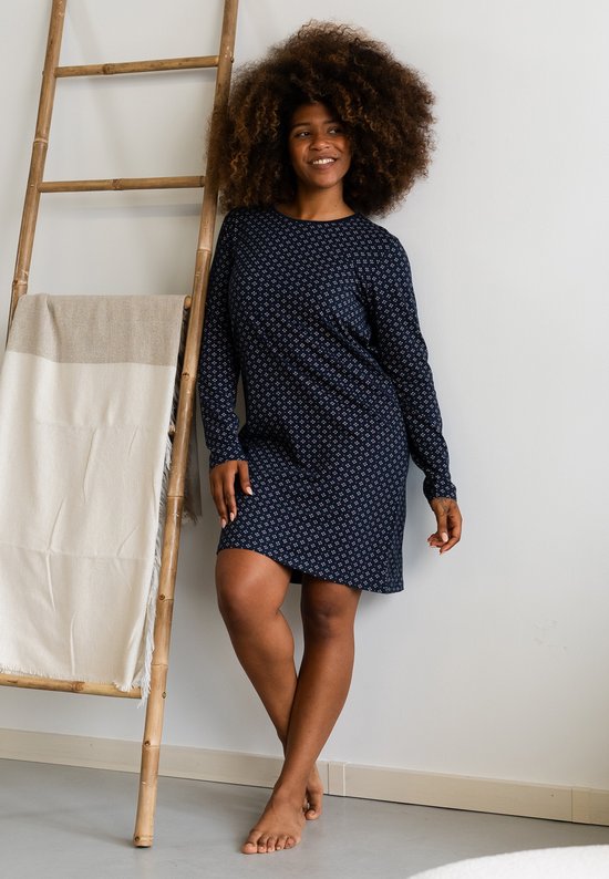Donkerblauw nachthemd met lange mouwen en een all-over patroon van kleine witte vierkantjes, gedragen door een vrouw die tegen een ladder leunt.