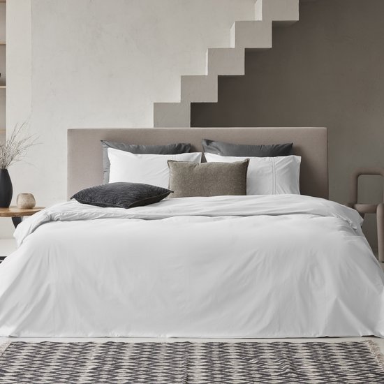 Couette blanche sur un lit avec divers coussins et un tapis ethnique.