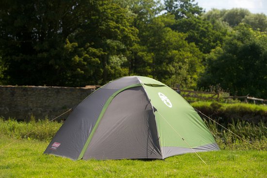 Groene en grijze Coleman Darwin 3 koepeltent op gras met bomen op de achtergrond.