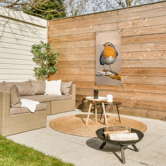 Tuinposter met roodborstje aan een houten schutting op een terras met loungeset en vuurschaal.