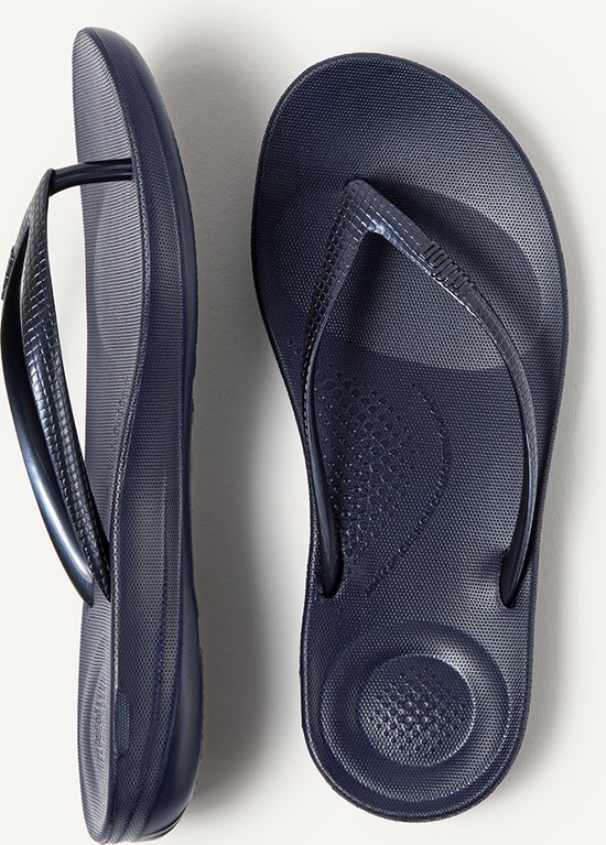 Paar donkerblauwe FitFlop teenslippers met een glanzend bandje, van bovenaf gezien.