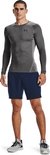 Man staat in grijze Under Armour tight fit longsleeve met zwart Under Armour logo en blauwe shorts.