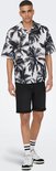 Man met palmbomenprint shirt en zwarte shorts.