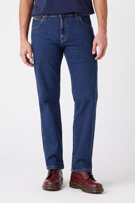 Blauwe Wrangler jeans, regular fit, gedragen met donkerblauwe T-shirt en rode schoenen.