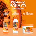 Shampoing, après-shampoing et masque capillaire Garnier Fructis Papaya Hair Food sur fond orange avec des morceaux de papaye.