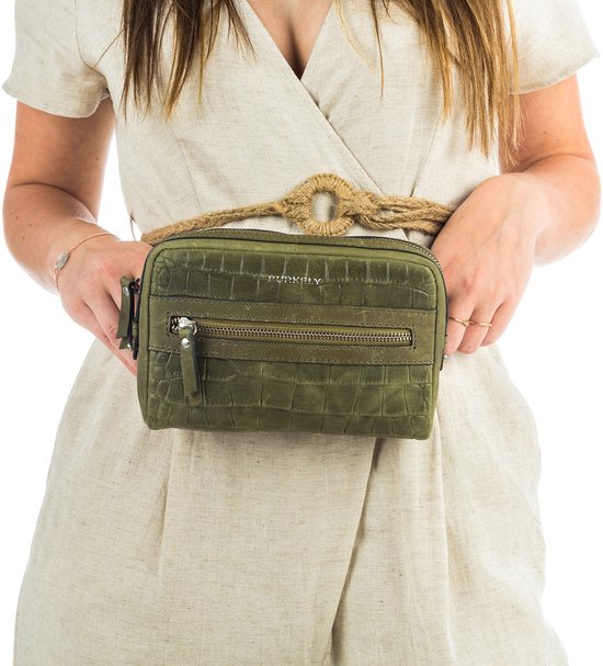 Groene croco print heuptas met twee ritsvakken, gedragen door een vrouw over een linnen jumpsuit.