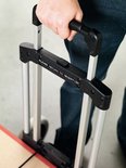 Hand met spijkerbroek pakt de metalen handgreep van een trolley met de tekst "PLEASE RETURN TO RECEPTION".