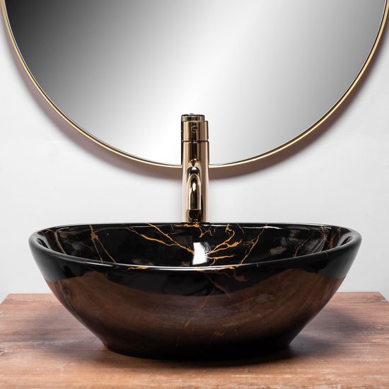 Lavabo noir avec imprimé marbre et veines dorées, robinetterie dorée. Miroir rond à bord doré.