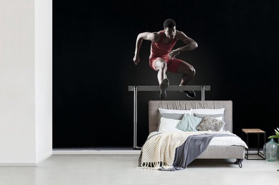 Athlète masculin saute par-dessus un obstacle de fotobehang
