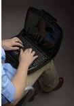 Persoon typt op laptop in zwarte hoes, die op schoot rust.