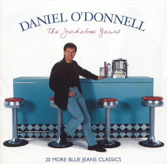 Daniel O'Donnell, 'The Jukebox Years'. Hij draagt een zwarte jas, blauwe jeans en zwarte schoenen. Hij zit op een rode barkruk aan een blauwe bar met een jukebox.
