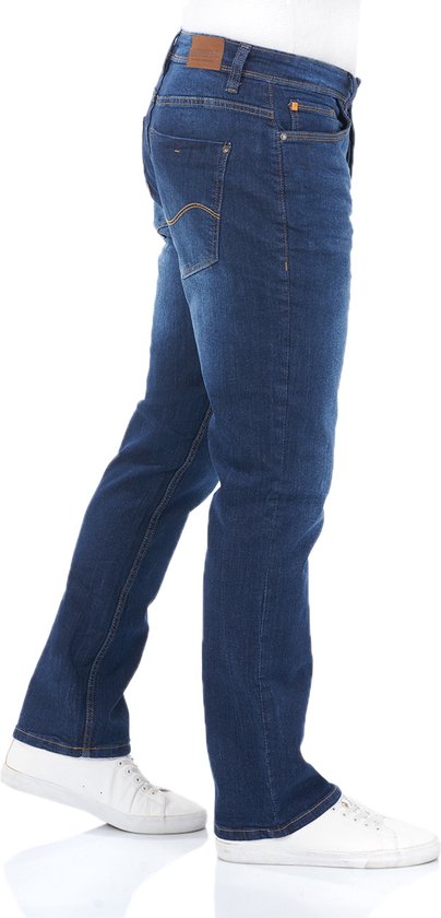 Man in profiel in een blauwe jeans met rechte pijpen en witte sneakers.