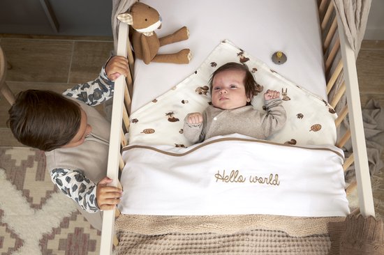 Baby in ledikant met deken met tekst "Hello world", kijkt naar ouder. Bosdiertjes print.