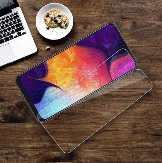 Transparante screenprotector voor smartphone op houten tafel naast laptop en koekjes.