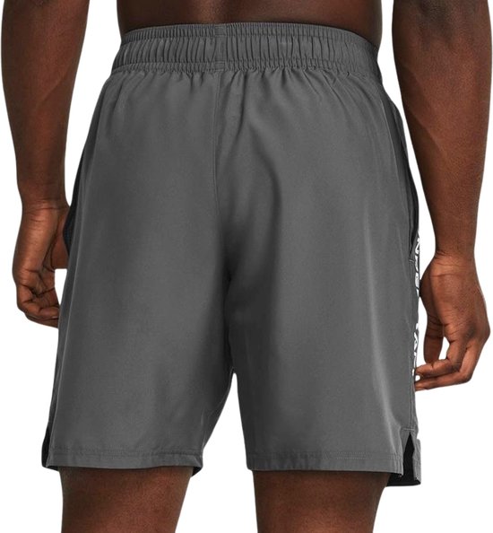 Grijze sportbroek van Under Armour met witte tekst op de zijkant, gedragen door een man.
