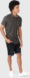 Jonge man in donkergrijs poloshirt, zwarte jeansshort met omgeslagen pijpen en witte sneakers.