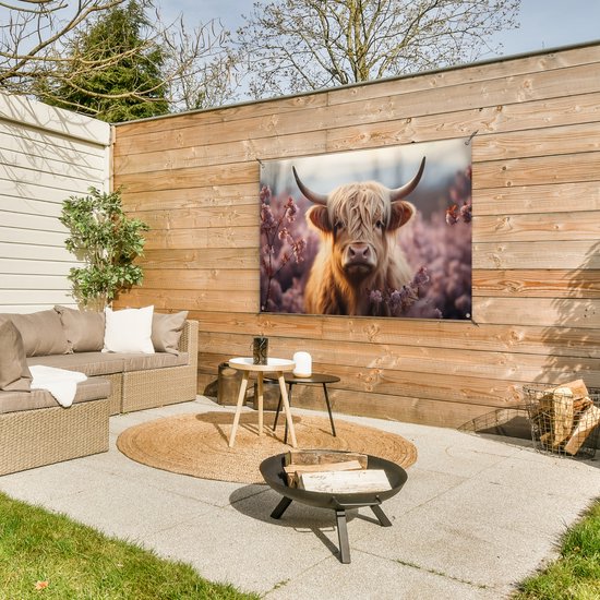 Een bruine Schotse hooglander in een veld met roze bloesems. De poster hangt aan een houten schutting op een terras met tuinmeubilair.