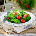 Een kom met rucola en cherrytomaatjes, versierd met een zilverkleurig patroon op de rand. Een vork ligt ernaast.