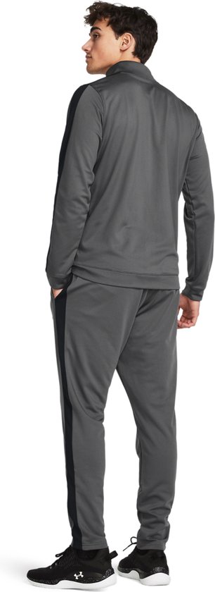 Achterkant van een man in grijs Under Armour trainingspak met zwarte streep op het been en de mouw.