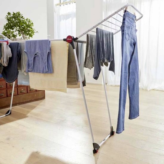 Étendage Vileda Infinity Flex rempli de divers vêtements comme des jeans, des pulls et des serviettes, dans un salon.