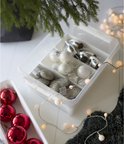 Transparante opbergdoos met kerstballen, kerstversiering en lichtjes, verdeeld in compartimenten.