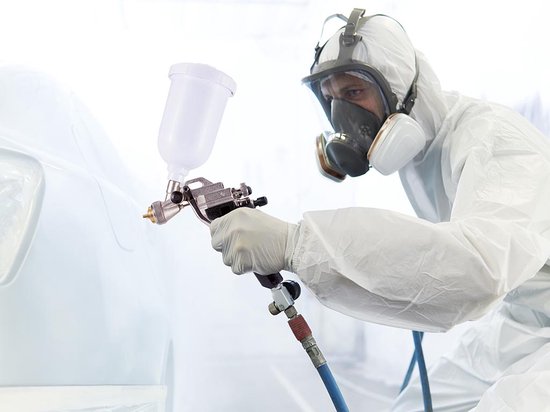 Persoon in wit beschermend pak en masker spuit een auto met een Stanley airbrush.