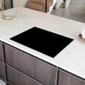 Zwarte inductiebeschermer op een marmeren aanrecht met houten kasten.