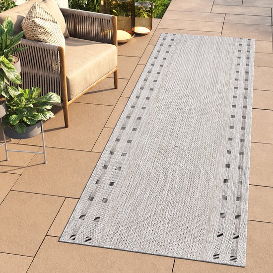 Un tapis de couloir gris, tissé, avec des rangées de petites rayures noires sur les côtés, posé sur une terrasse carrelée à côté d'un ensemble de salon.