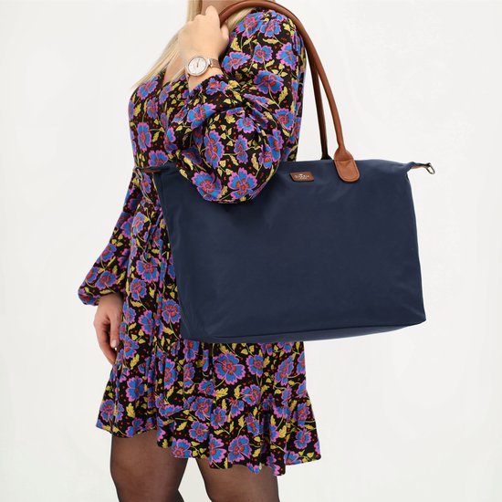 Model met bloemenjurk, draagt een donkerblauwe nylon tas met bruine handvatten.