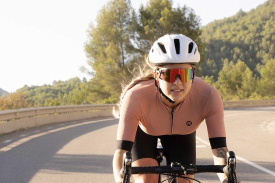 Vrouw op fiets draagt een zwarte Rogelli Sabre sportbril met gespiegelde rode lenzen en een roze fietsjack.