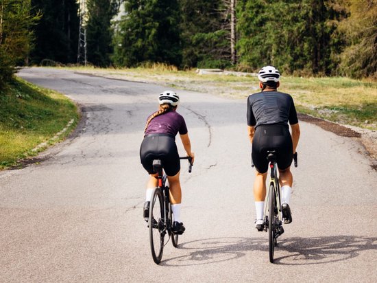 Twee fietsers rijden op een asfaltweg, weg van de camera.