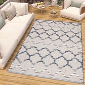 Een tapijt met een geometrisch patroon in blauw, grijs en beige, geplaatst op een houten terras naast een sofa.