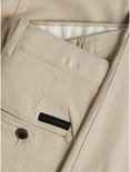 Detail van beige chino broek met bruine knoop en donker label op de achterzak.