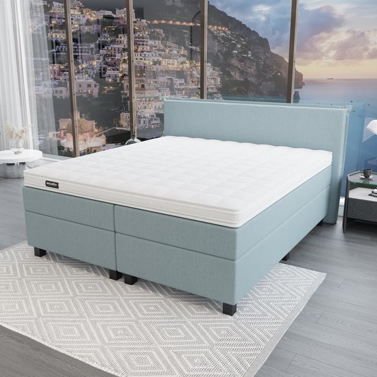 Lichtblauwe boxspring met matras op een grijs tapijt, met uitzicht op een stad.