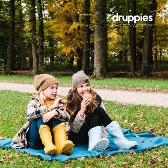 Twee meisjes met laarzen, zittend op een deken in het bos met herfstkleuren.