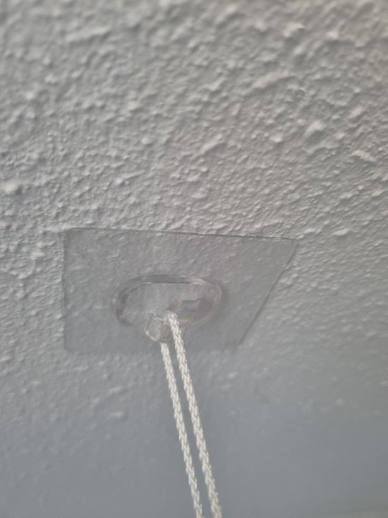 Transparante plakhaak met witte touwtjes bevestigd aan een gestructureerde muur.
