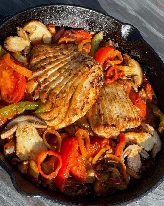 Gebakken vis met paprika, champignons en tomaten in een pan.