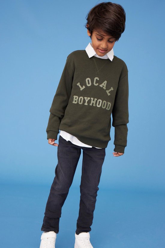 Jongens model in een donkergrijze slim fit jeans en een wit overhemd.