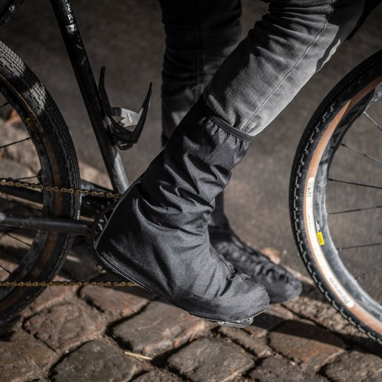 Een persoon op een fiets, draagt zwarte waterdichte fietsoverschoenen.