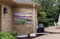 Een tuinposter van een paarse lavendelweide bij zonsondergang, aan de muur van een bakstenen huis naast een barbecue.