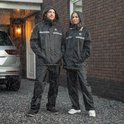 Man en vrouw in zwarte regenpakken met capuchon, staand in de regen.