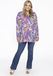 Vrouw draagt een paars shirt met bloemenprint en een spijkerbroek met witte platform sandalen.