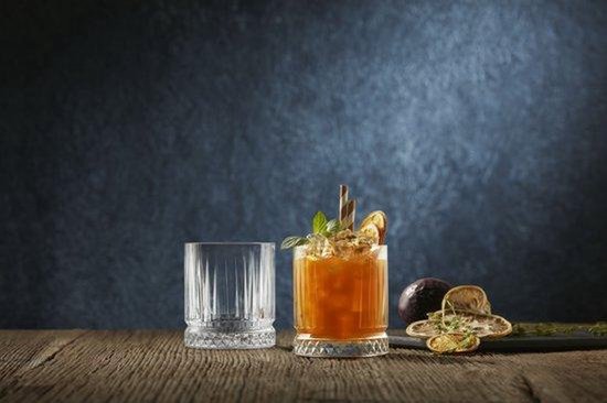 Twee glazen op een houten tafel, één met een oranje drankje en garnering, de ander leeg.
