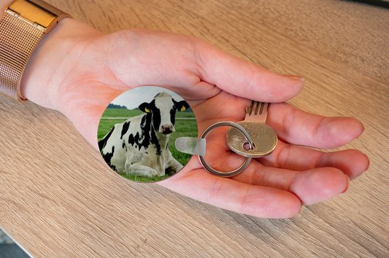Ronde sleutelhanger met een liggende zwart-witte koe in een weiland, in een hand.